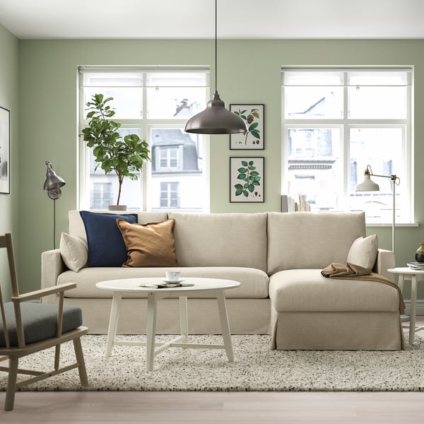 Cozy living room with beige HYLTARP sofa, cushions, green wall, coffee table, plant, lamp, two windows.
