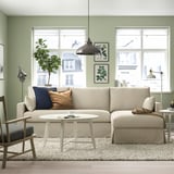 Cozy living room with beige HYLTARP sofa, cushions, green wall, coffee table, plant, lamp, two windows.
