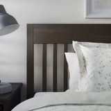 Modern bedroom with dark wood-platform bed, patterned pillow, nightstand, and wall lamp.