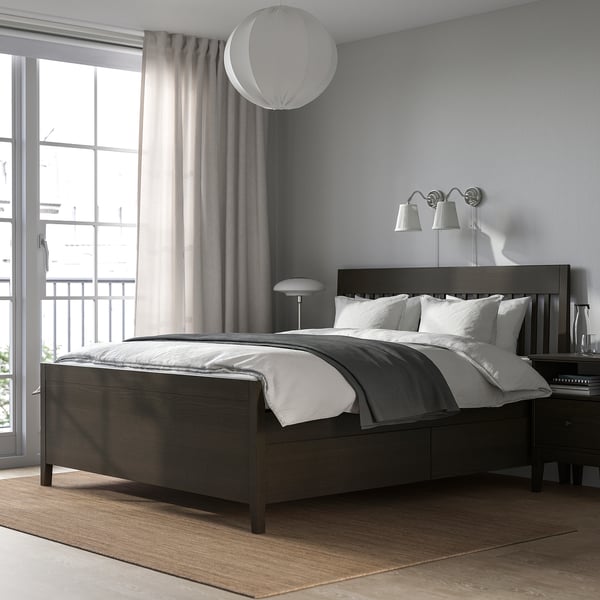 Modern grey bedroom with IDANÄS dark wood bed, large cushions, wall lamps, sleek rug, and large window with sheer curtains.