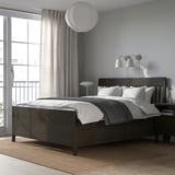 Modern grey bedroom with IDANÄS dark wood bed, large cushions, wall lamps, sleek rug, and large window with sheer curtains.