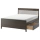 This image shows an IDANÄS bed frame in black with under-bed storage drawers. It has a wooden headboard with vertical slats and tapered legs.