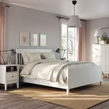 Modern bedroom with white IDANÄS bed, drawers, lamps, and plant. Light grey walls, cream curtains, artwork, and area rug.