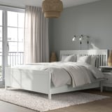 Modern bedroom with white IDANÄS bed, blue walls, large window, pendant & wall lamps, plush rug. Bed larger than side table.
