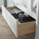 A white wooden drawer under a bed neatly holds folded gray towels.