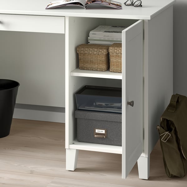 White desk with open door revealing storage: wicker baskets, magazines, and boxes.