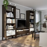 Dark wood bookshelves with books & decor, large tv, beige carpet, white couch, black coffee table, grey walls, large window.