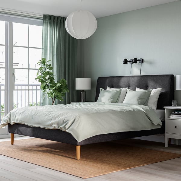 Modern bedroom with IDANÄS grey bed, striped pillows, nightstand, green curtains, plant, rug, pendant light.