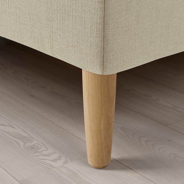 Close-up of upholstered bed corner, showcasing soft beige fabric and sturdy wooden leg.