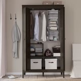 IDANÄS dark wood wardrobe with clear doors, organized clothes, hangers, and storage boxes.