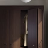 Dark brown wooden wardrobe with one open door revealing hanging coats, silver handles.