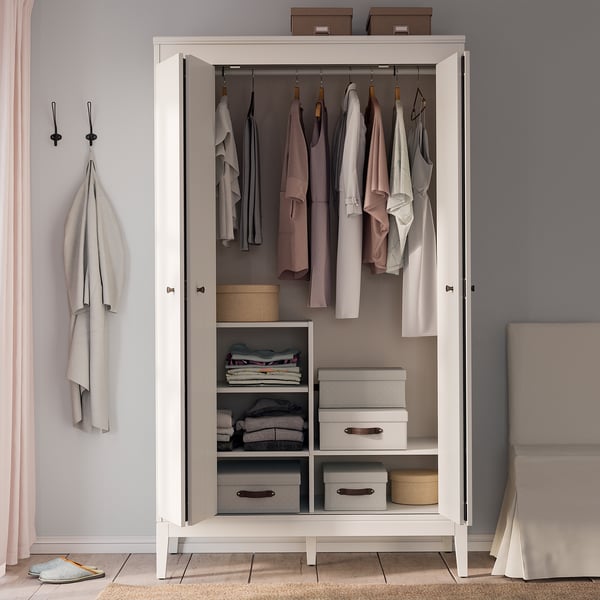 A white IDANÄS wardrobe with open bifold doors displaying clothes and organized storage boxes inside.