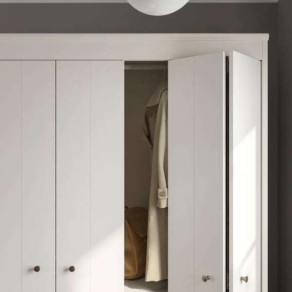 Modern white wardrobe with bifold doors, partially open revealing hanging coat, sleek design with silver handles.