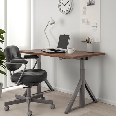 Adjustable IDÅSEN desk in home office with chair, laptop, lamp, and mug.