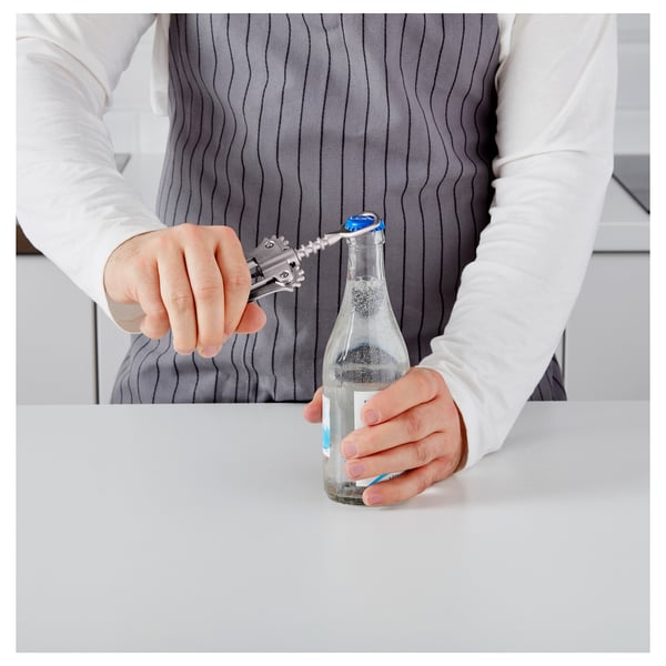 Person uses corkscrew to open wine bottle on white table.