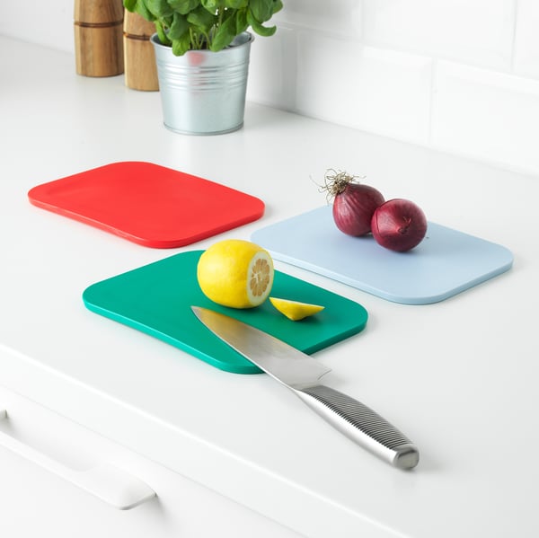 Three colorful cutting boards on a white countertop: red, blue, and green. One has onions, another has a lemon and knife.