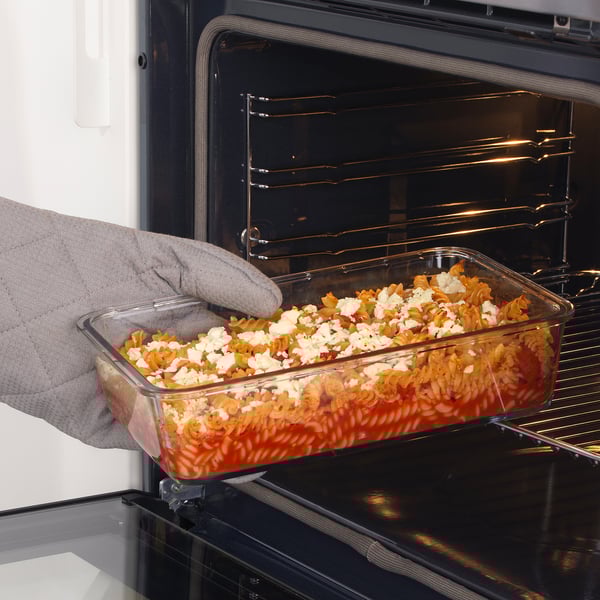 Person placing glass container with food into oven. Oven-safe design for reheating leftovers.