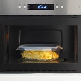 A microwave with an oven-safe glass food container inside, heated, showing a transparent lid and snap-and-lock feature.