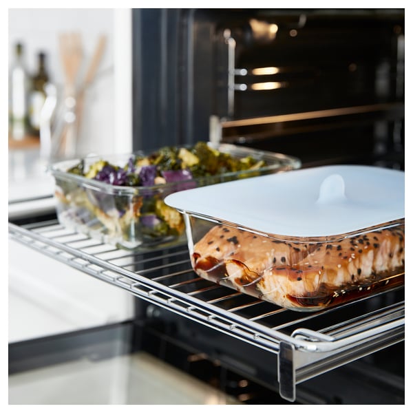IKEA 365+ glass food container with lid inside oven, holding cooked salmon and vegetables.