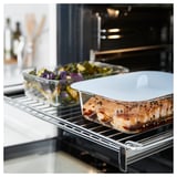 IKEA 365+ glass food container with lid inside oven, holding cooked salmon and vegetables.