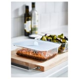 Glass IKEA 365+ food container with lid holding cooked salmon, next to veggies and bottles.