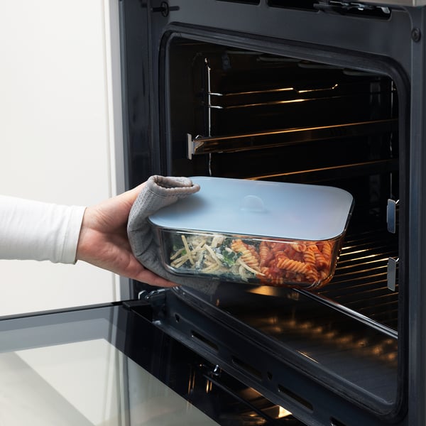 Person placing glass food container with lid into oven, showcasing oven-safe feature.
