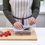 Person placing a lid on a container of leftovers on a wooden cutting board with a knife and tomatoes nearby.