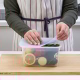 Person storing food in clear IKEA 365+ container with vacuum-sealing lid on wooden board.