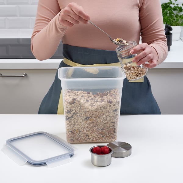A person is scooping granola from a clear IKEA 365+ container on a kitchen counter, which has a snap-lock lid ensuring freshness and preventing leaks.