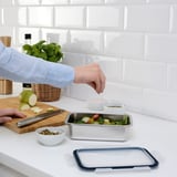 Person prepares salad in stainless steel ikea container on kitchen counter.