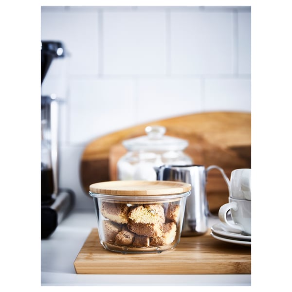 Clear glass jar with bamboo lid full of cookies on wooden counter. Coffee maker behind.