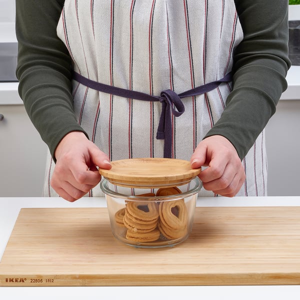 Person placing lid on glass jar filled with cookies on wooden board.