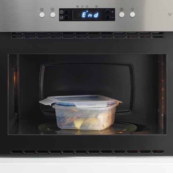 Microwave with clear container of leftovers inside, showing heating function.