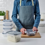 A person in an apron uses stackable, clear food containers with snap-lock lids, keeping leftovers fresh and organized.