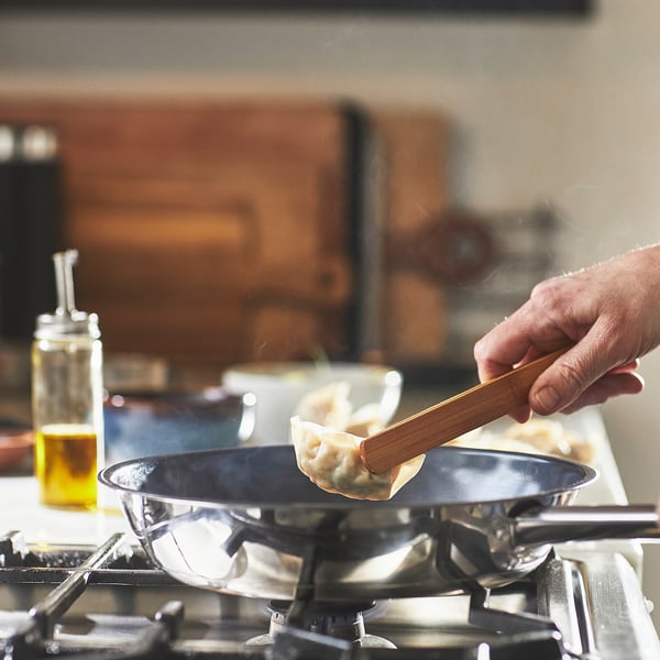 Hand flips dumpling in non-stick pan on gas stove.