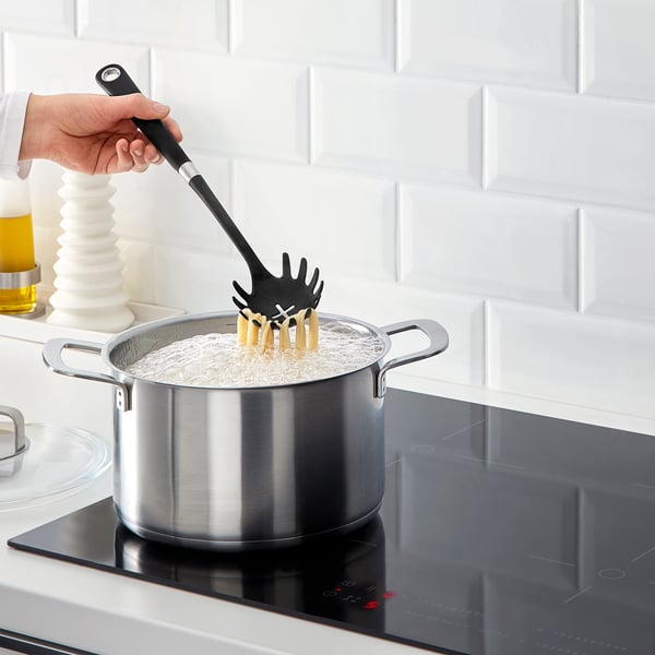 Person cooking pasta using IKEA pasta server in a modern kitchen.