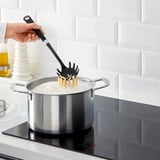 Person cooking pasta using IKEA pasta server in a modern kitchen.