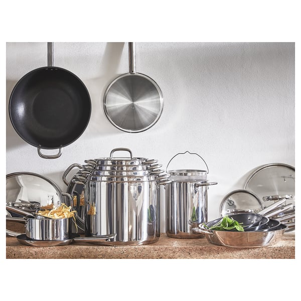 Stainless steel ikea cookware set on wooden table, with lids and utensils. Modern design.