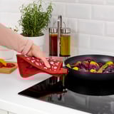 Person cooks colorful vegetables in a skillet using a red mitt to handle the pan.