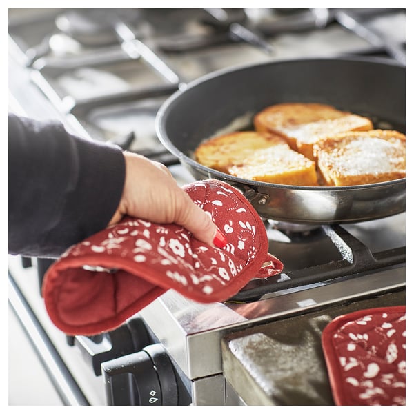 Person cooking with red INAMARIA kitchen glove on gas stove, using skillet with bread.