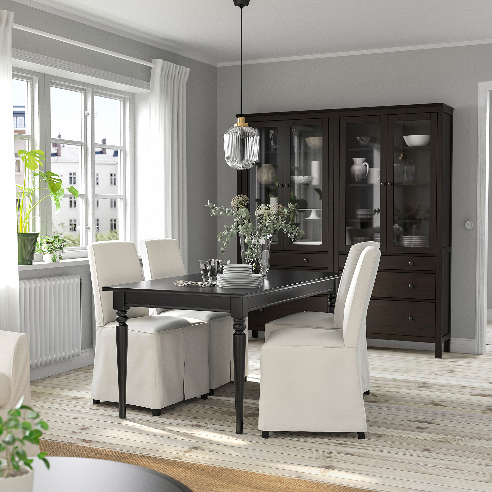 Modern dining area with black extendable table, white chairs, dark cabinet, and city view window.