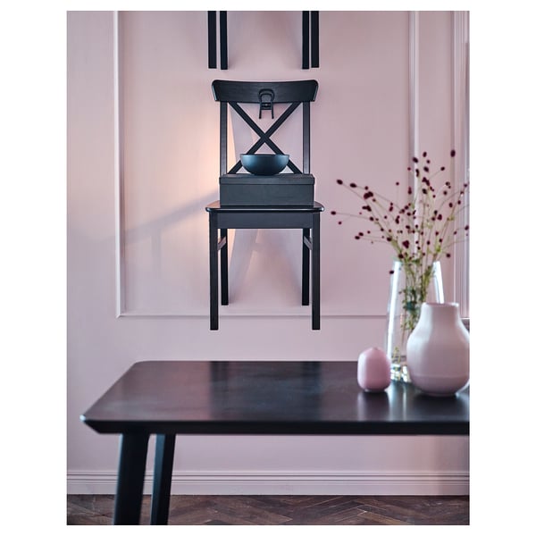 A stylish black INGOLF dining chair with a high back and wooden seat. It sits beside a dark table with a pale pink vase and decorative branches.