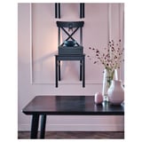 A stylish black INGOLF dining chair with a high back and wooden seat. It sits beside a dark table with a pale pink vase and decorative branches.