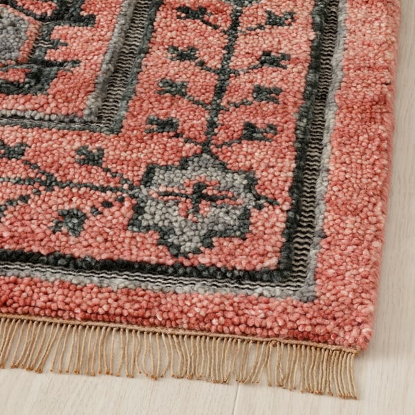 Textured, hand-knotted wool rug with intricate geometric patterns, fringed edges, on wooden floor.