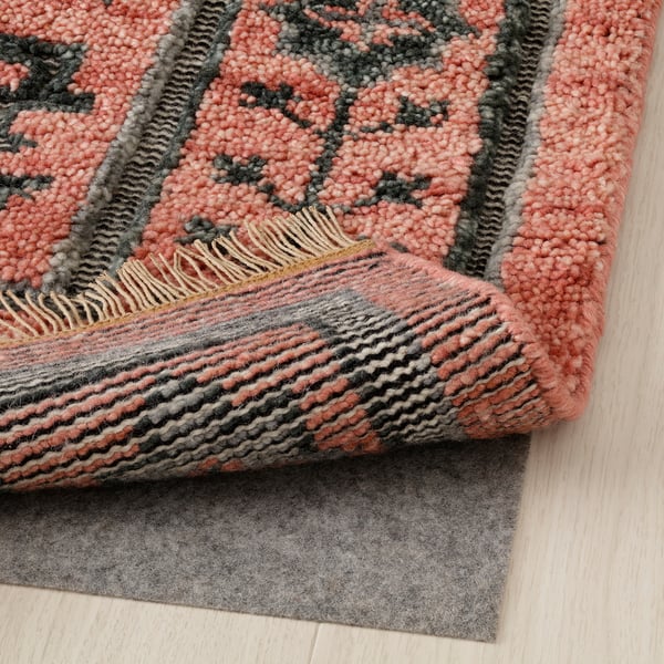 Textured red and gray woven rug with fringe, folded to reveal soft backing and non-slip mat underneath.