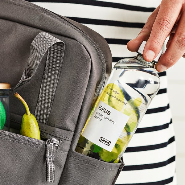 Person placing lemon-lime bottle into backpack with fruits.