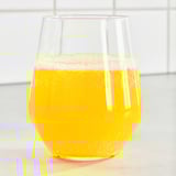 Clear glass cup filled with bubbly, orange-colored ISKUB drink, placed on a surface. Key ingredients: orange flavoring, sweeteners, low sugar.