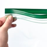 A hand holding a transparent, reusable green food storage bag, demonstrating its sealable and flexible nature.