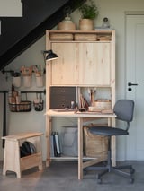 Home office with IVAR natural wood desk and chair, organized with storage baskets, art supplies, and a lamp under stairs.