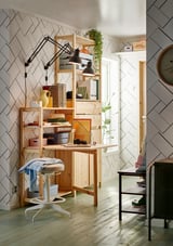Home office with light wood IVAR desk, stool, lamp, and colorful items.